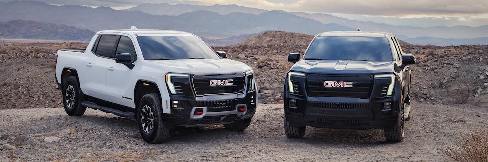 A white and a black GMC pickup trucks parked in the desert
