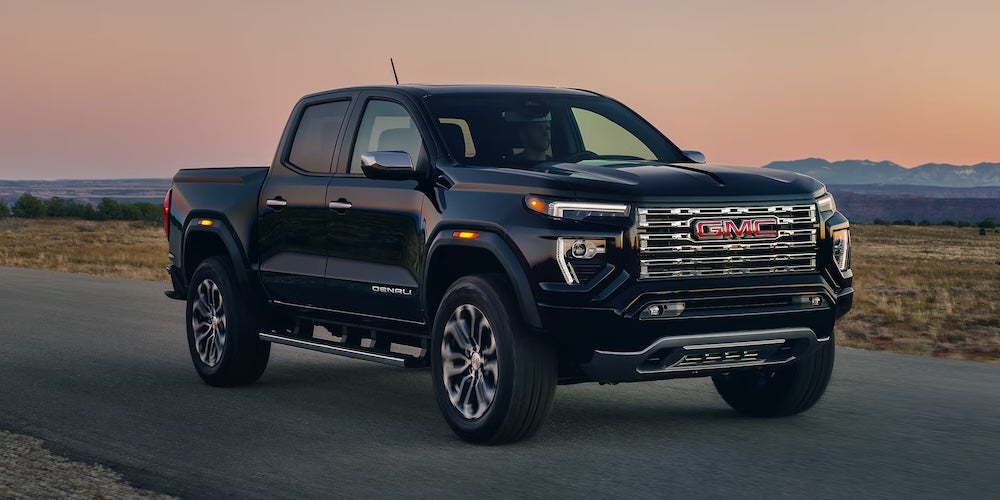 A black GMC pickup truck on a desert road at sunset